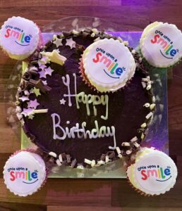 A birthday cake surrounded by cu0pcaks with the charity logo displayed on them.