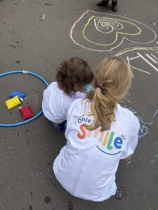 Two children crcohed down looing away from camera writing and drawing in chalk on the floor.