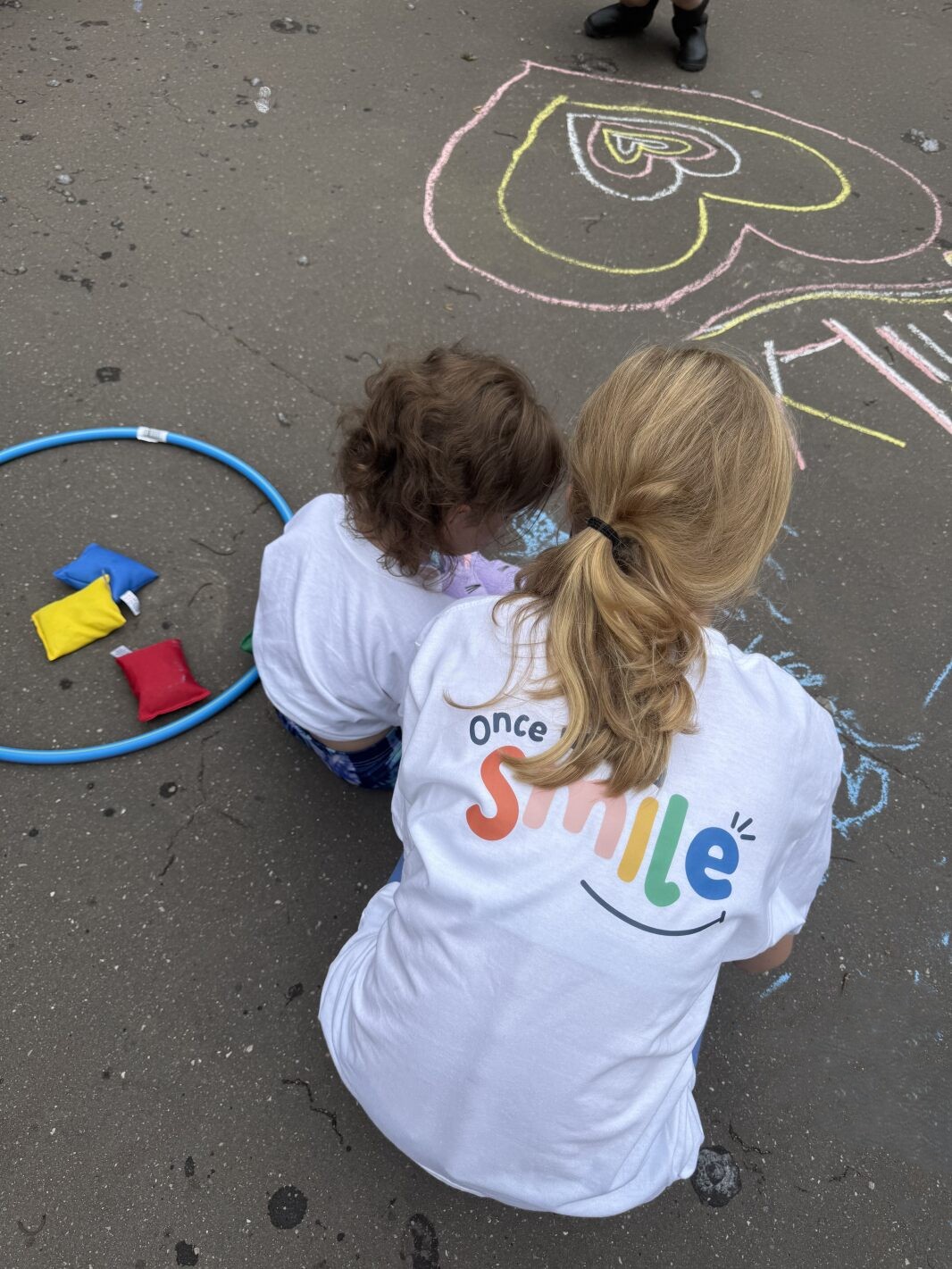 Two children crcohed down looing away from camera writing and drawing in chalk on the floor.